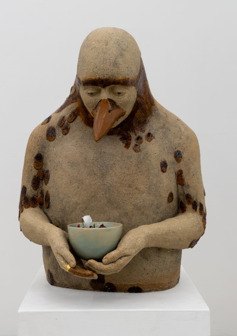 Fotografi av keramikskulptur av en människokropp med näbb. I händerna håller figuren en skål.