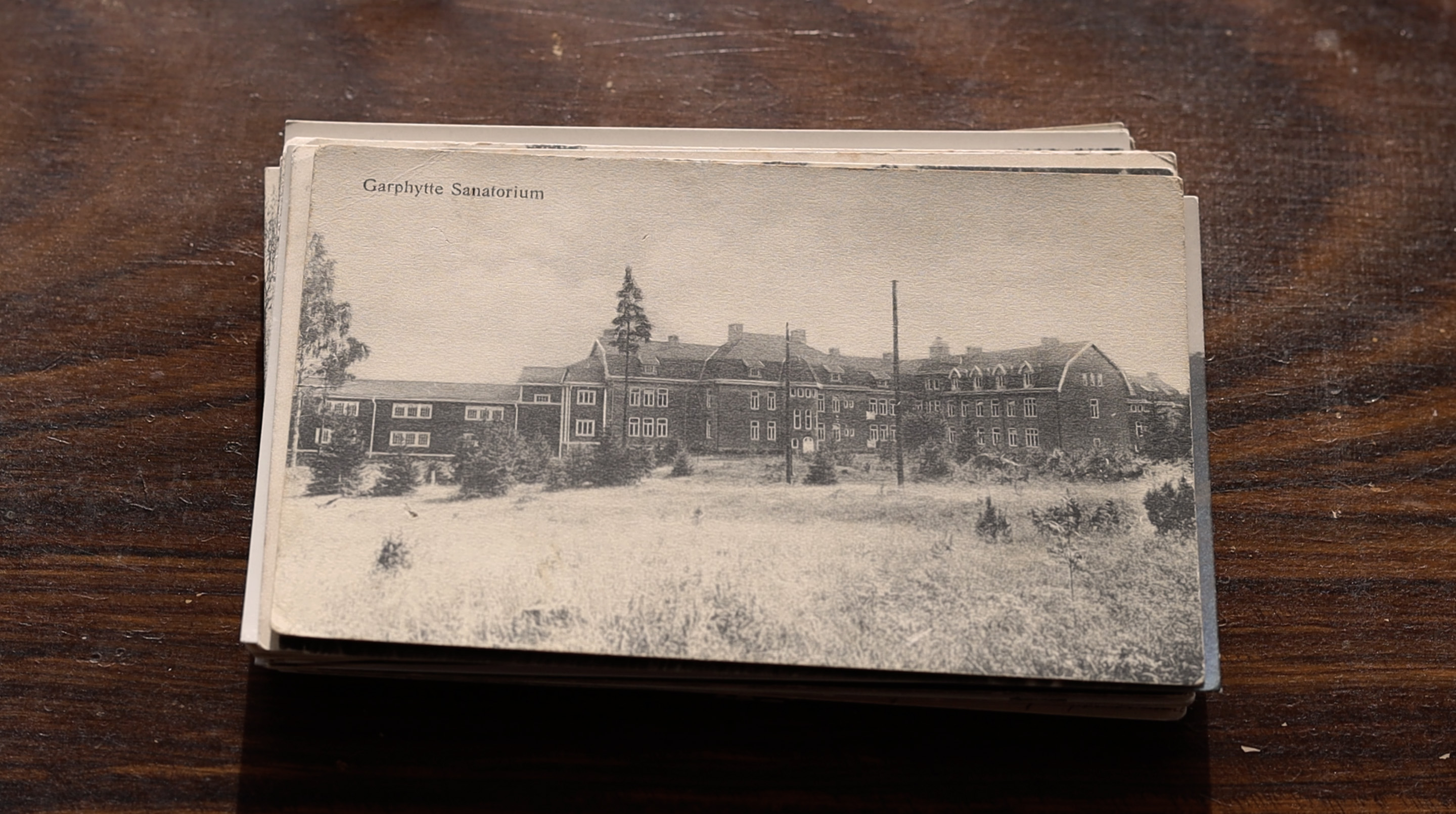 Fotografi av en hög med gamla svartvita vykort. Det översta kortet avbildar en stor byggnad.