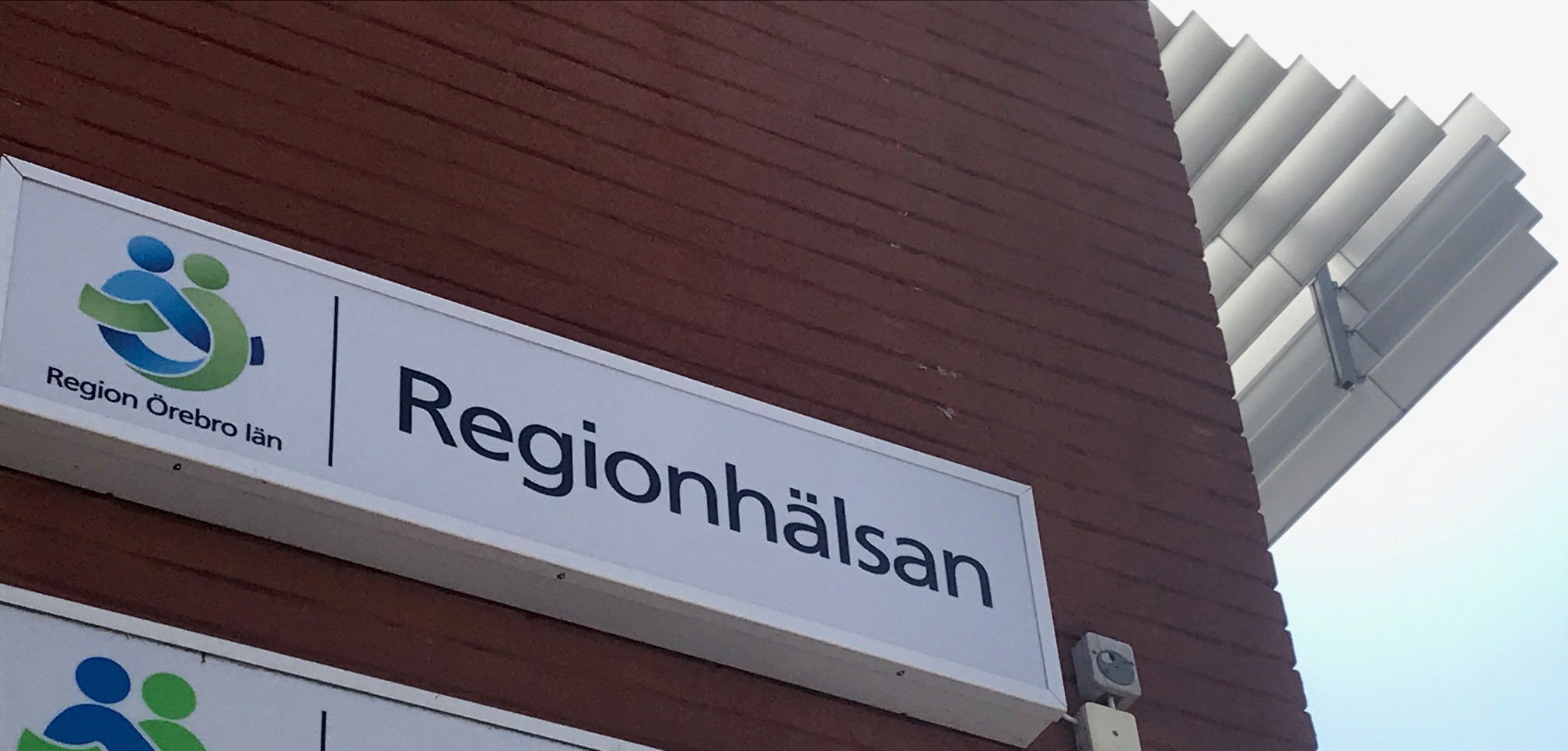 Fasadskylt med Regionhälsans logotyp på en röd tegelvägg