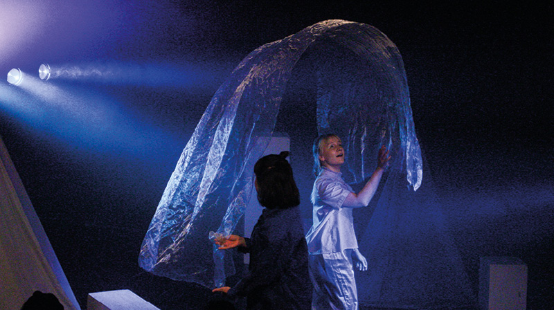 Två dansare i blått ljus med genomskinlig sjal som svävar ovanför dem